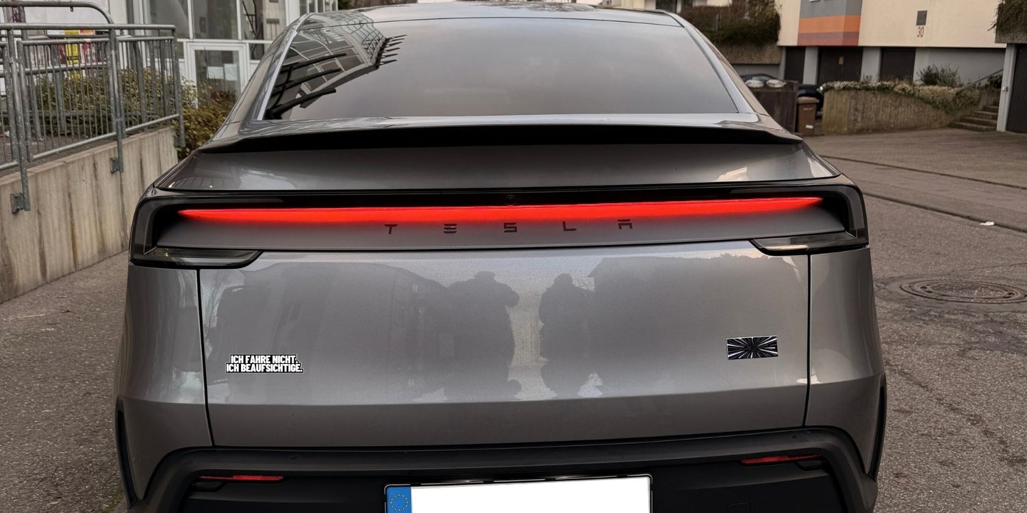 Sticker „Ich fahre nicht. Ich beaufsichtige.“ links auf der Heckklappe eines Model Y Juniper, Ansicht gerade von hinten