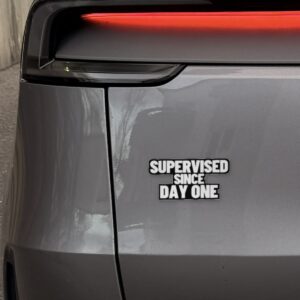 Sticker „Supervised since day one“ links auf der Heckklappe eines Model Y Juniper, neben dem Rücklicht