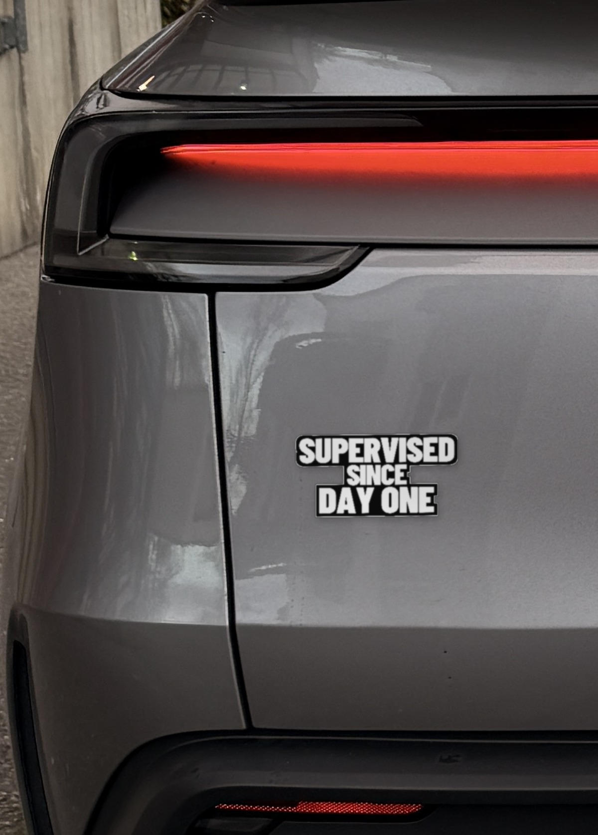 Sticker „Supervised since day one“ links auf der Heckklappe eines Model Y Juniper, neben dem Rücklicht