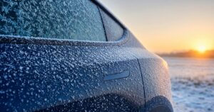 Vereister bündiger Türgriff an einem dunkelblauen Elektro-SUV mit Raureif, im Hintergrund Sonnenaufgang über frostigem Feld